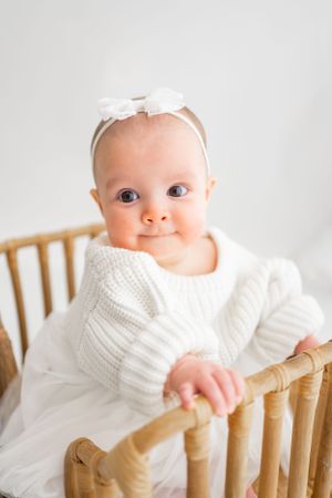 Baby in white sweater posing on wooden chair during professional photoshoot.