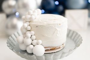 White frosted cake with pearl decorations on silver platter against dark background.
