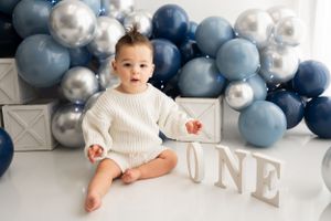 Navy and silver balloon garland decorates white backdrop with 'ONE' text display.