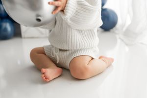 Close-up of tiny bare feet and white knit clothing against white floor.
