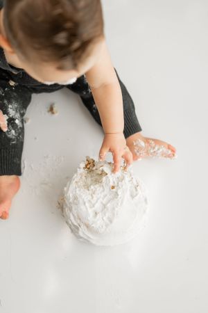 Overhead view of small child touching white frosted cake during messy cake smash session.