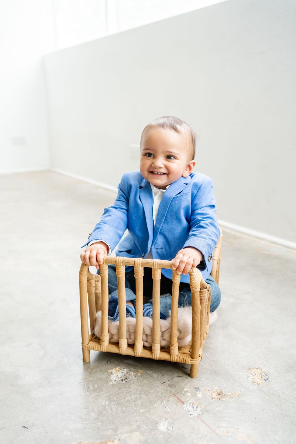 Toddler in light blue outfit holding onto a wooden crib railing while smiling warmly.