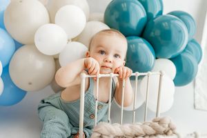 Blue and white balloon decorations create a festive backdrop for a celebratory moment with a white crib.