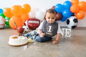 Sports-themed first birthday setup with blue and orange balloons and decorative sports equipment.