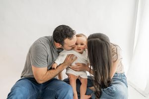 A family embraces and plays together on a white couch in a heartwarming lifestyle moment.