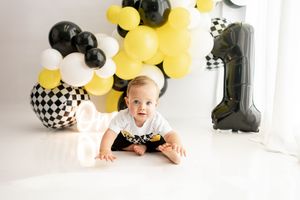 Yellow and black party balloons create a festive backdrop for a fun first birthday celebration photoshoot.