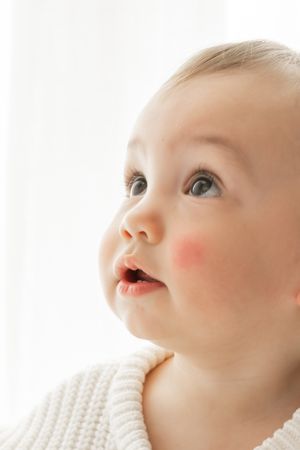 Close up details of a baby's face in white knitted clothing against bright background.