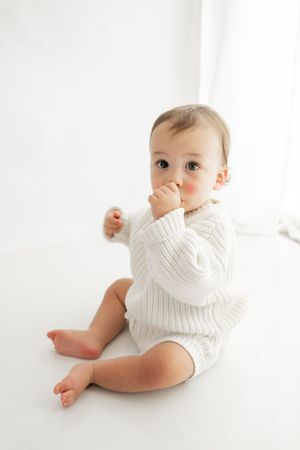 Small figure in white knit sweater reclining against white background showing playful movement.