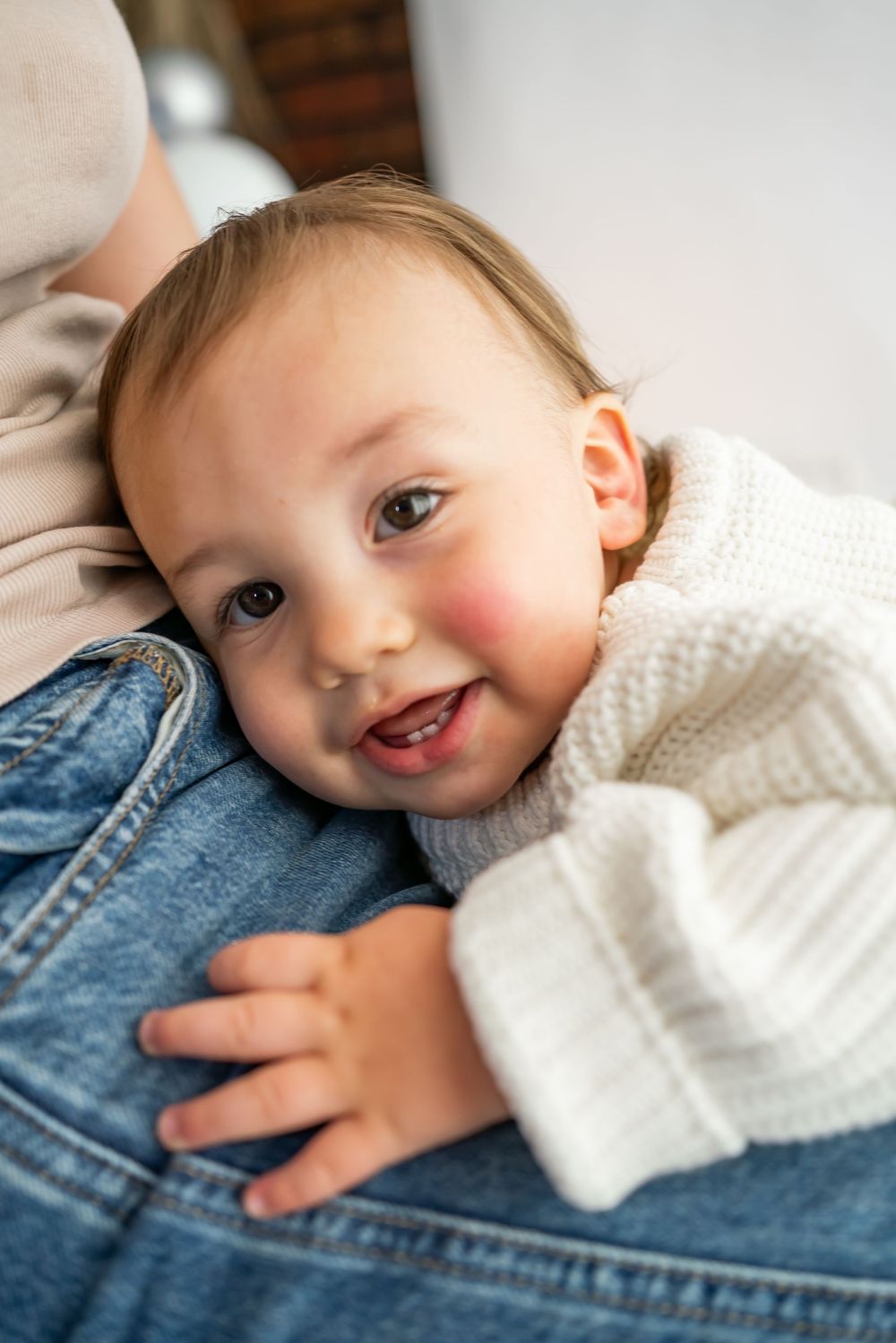 Close up of small figure in white knit sweater laying on denim surface with joyful expression.