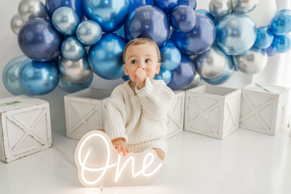 Blue and white balloon arch decor and white text reading 'One' create an elegant first birthday celebration setting.