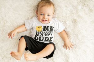 Baby wearing "One Cool Dude" t-shirt lying on white furry rug.