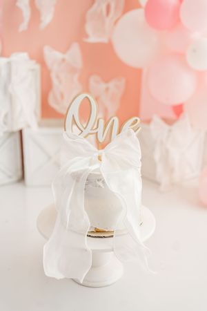 White leather baby shoes with bow details sit on white surface against soft coral background.