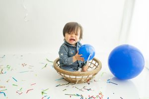 Colorful balloons and confetti create a festive party scene with a yellow platform against a white background.