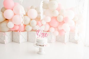 Elegant white and pink balloon arch installation with soft romantic lighting in a light-filled room.