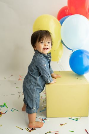 A playful party scene features red, yellow and blue balloons with scattered confetti on the floor.