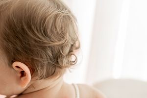 Two young siblings sitting together and looking at each other against a bright white background.