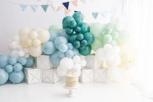 Party decorations with blue and teal balloon garlands and bunting flags hanging against a white wall.