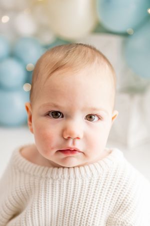 Four close-up portraits of a baby wearing a white knit sweater against a soft blurred blue and white background.