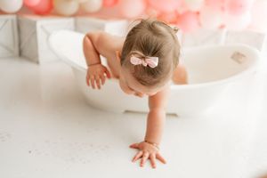 Cute baby practicing adorable crawling moves on white carpet with toy blocks and balloons in background.