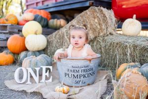 Baby sits in vintage metal pumpkin container surrounded by fall decor.