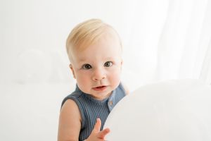 A small child in a blue and white striped romper looks off to the side against a light background.