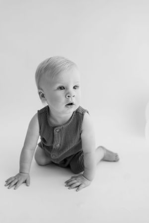 A sequence of black and white photos showing a baby in a striped romper crawling on a white background.