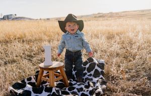 Child in cowboy outfit celebrating first birthday in golden field setting.