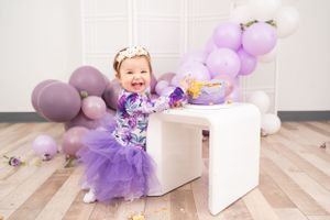 Purple balloon decorations and tulle dress create festive birthday celebration scene.