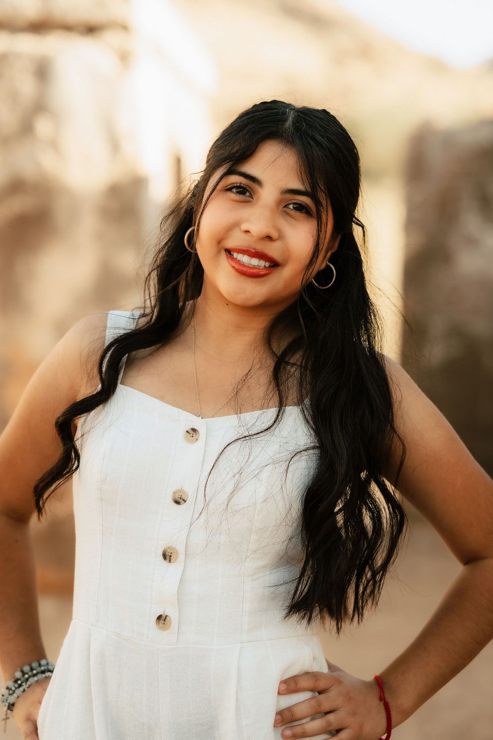 Portrait of woman in white button-front sundress with long dark hair smiling outdoors during golden hour.