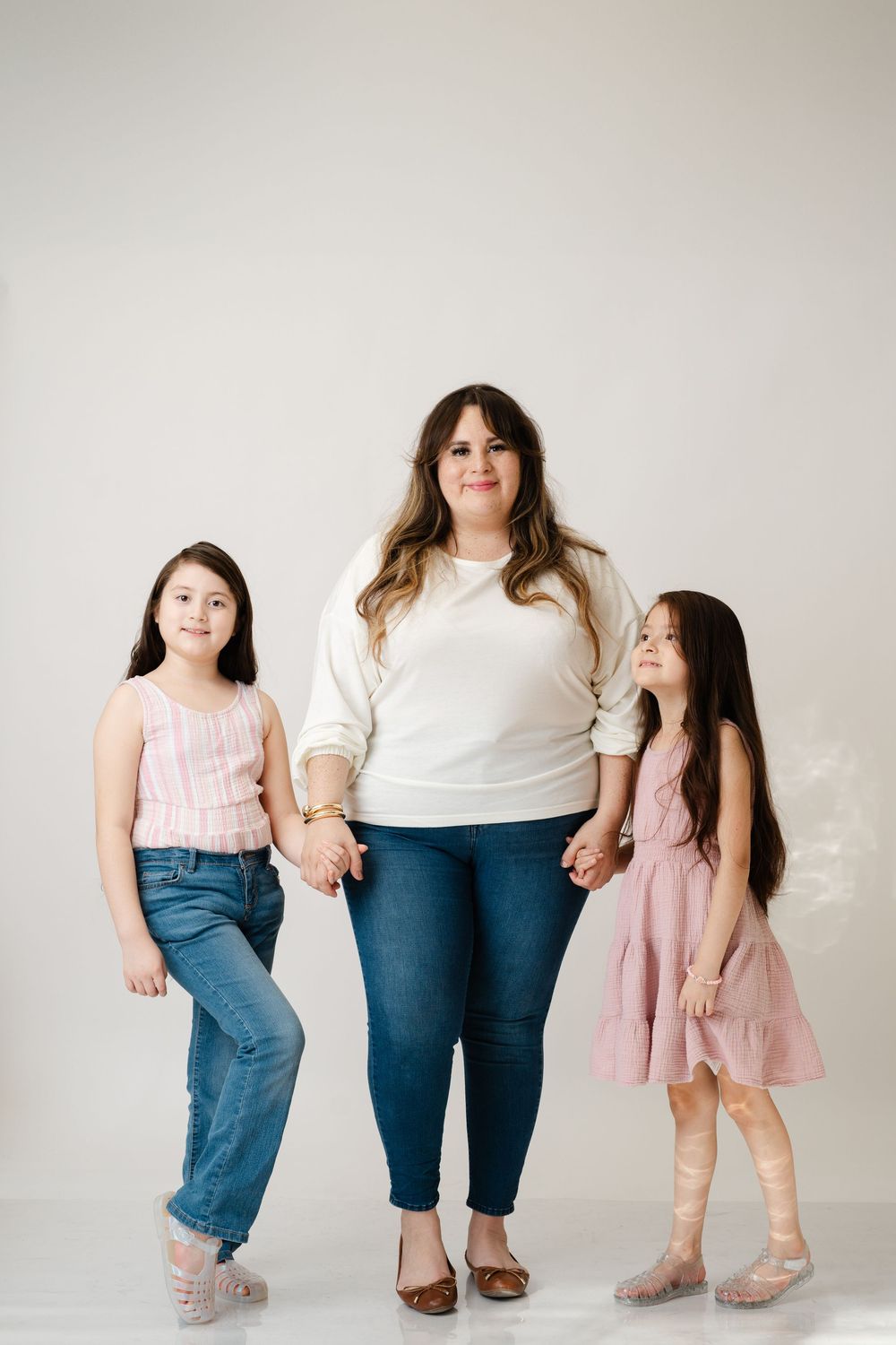 A warm family portrait of three generations standing together in casual attire against a neutral background.