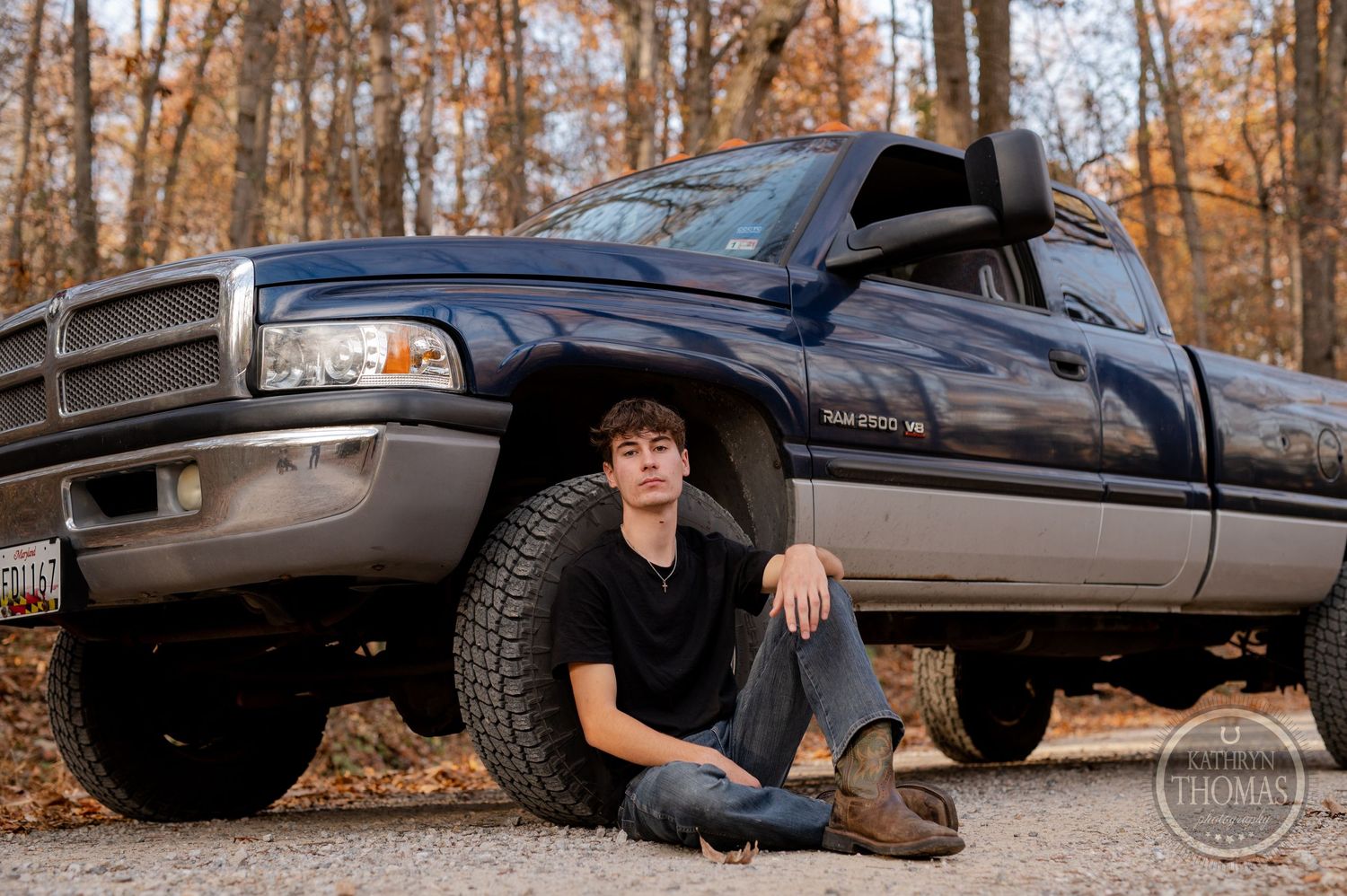 Low angle shot of person sitting beside lifted Dodge Ram truck on autumn forest trail.