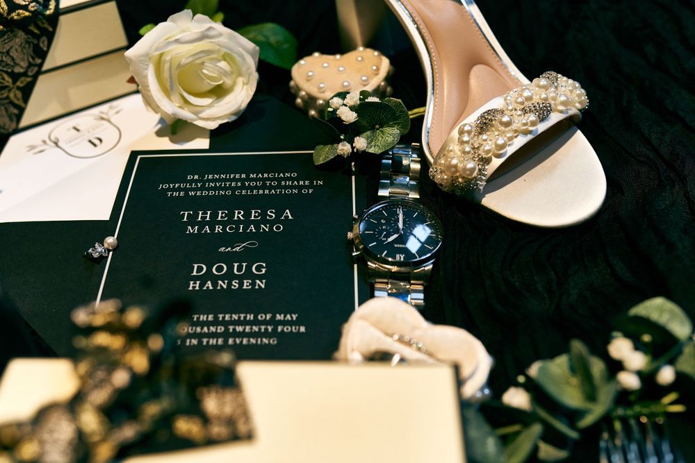 Wedding details featuring black invitation, pink rose, and crystal-embellished bridal shoe.
