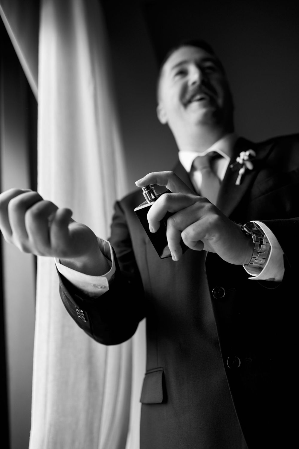 Black and white image of groom showing cufflinks in window light.
