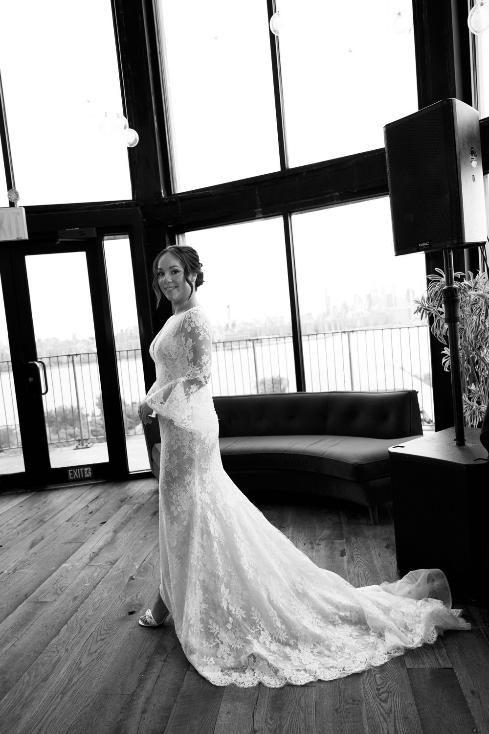 Black and white bridal portrait in lace gown with dramatic train beside window.
