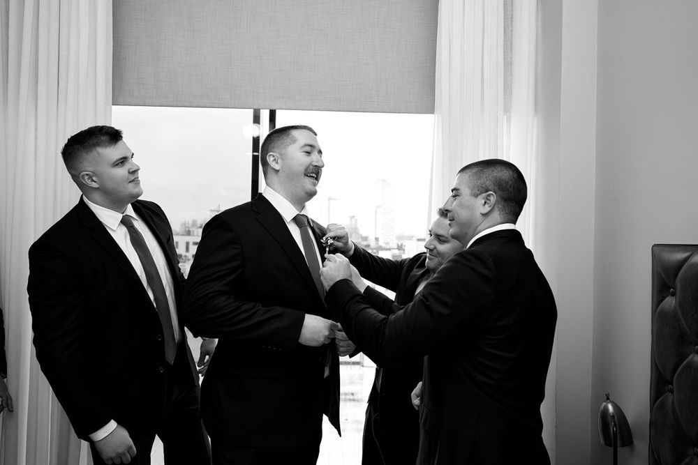 Groomsmen in black suits shown in dynamic black and white composition during wedding preparations.