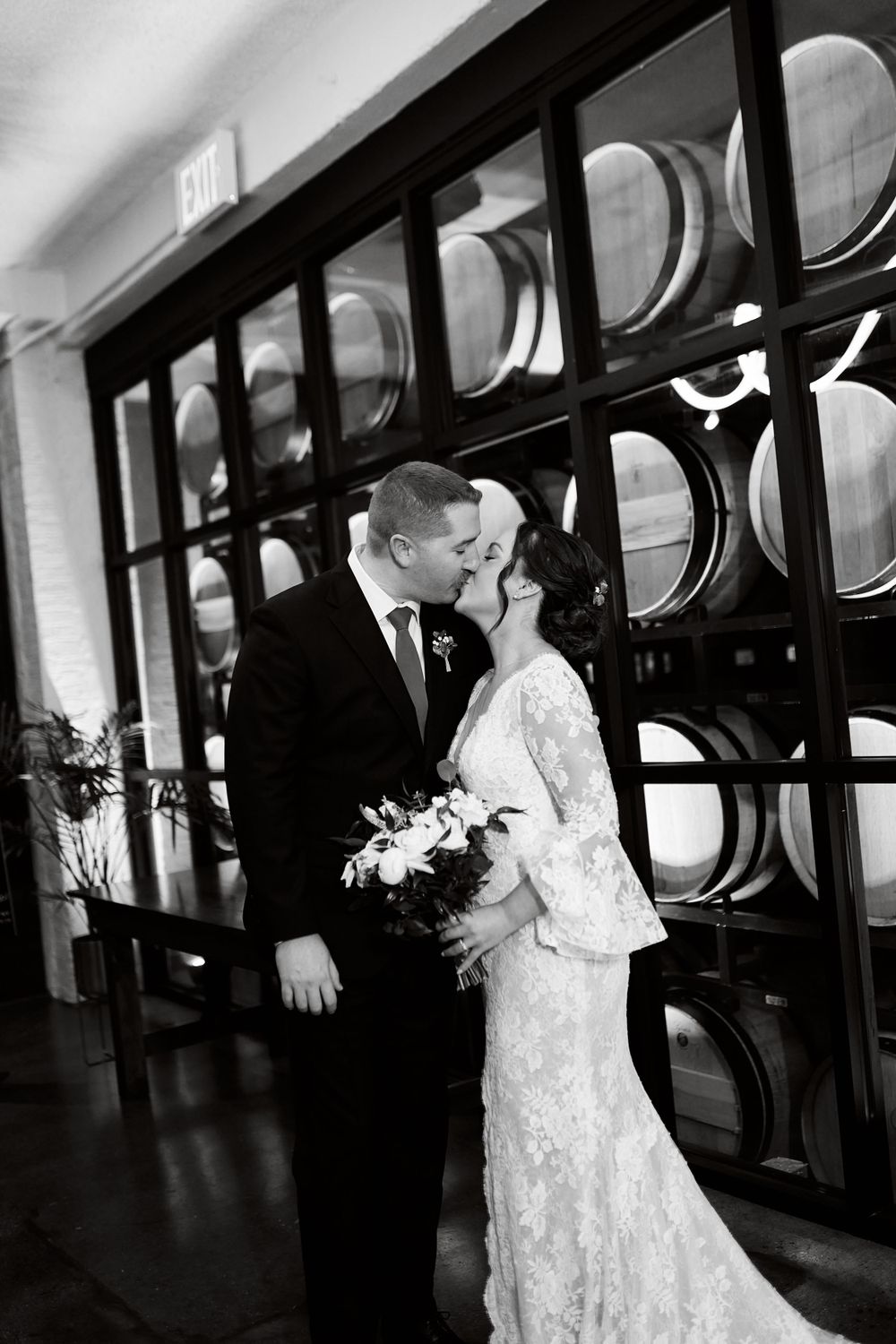 Wedding couple embraces in front of glass windows in a modern building hallway.