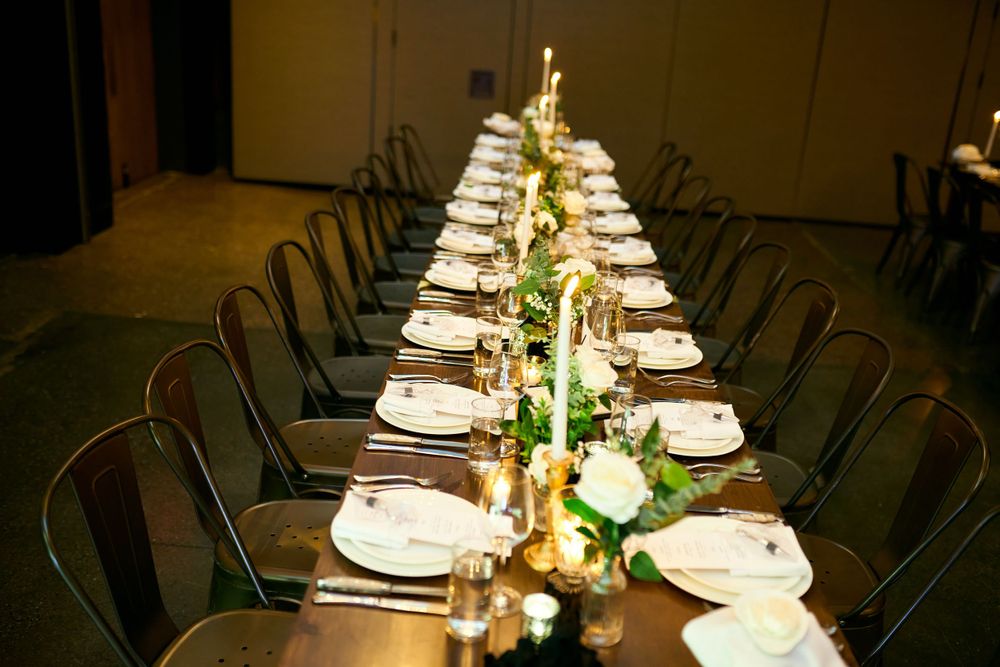 Long dining table elegantly set with white linens and centerpieces for wedding reception.