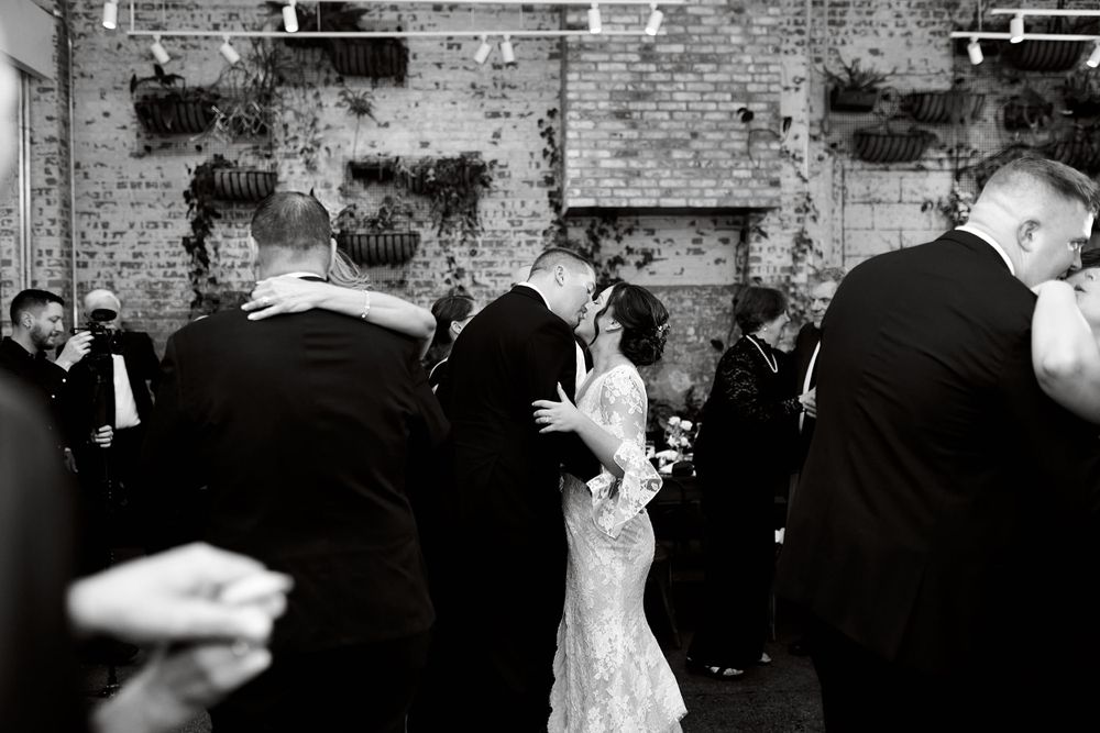 Wedding party gathered against textured brick wall for formal photographs.
