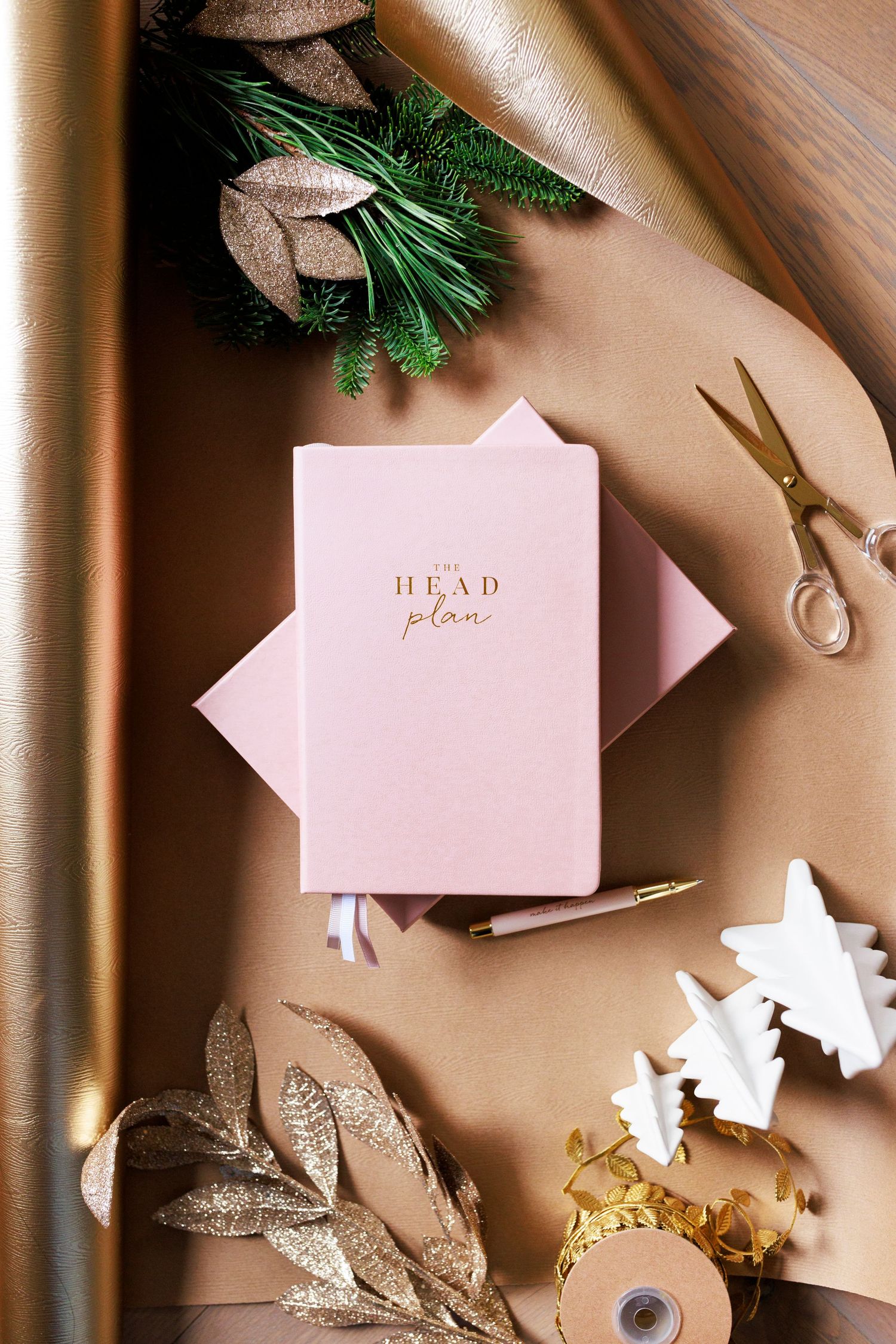 Pink planner with gold text surrounded by decorative leaves and scissors.