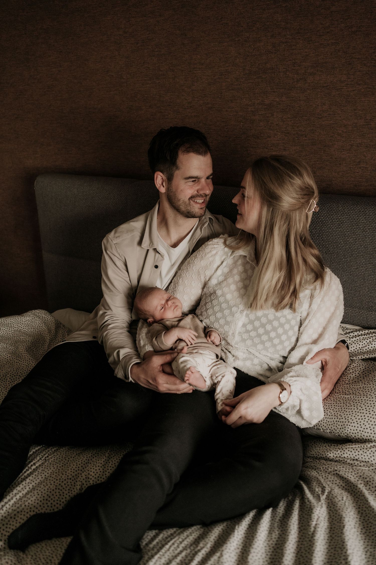 Papa en mama zitten op bed met hun pasgeboren baby