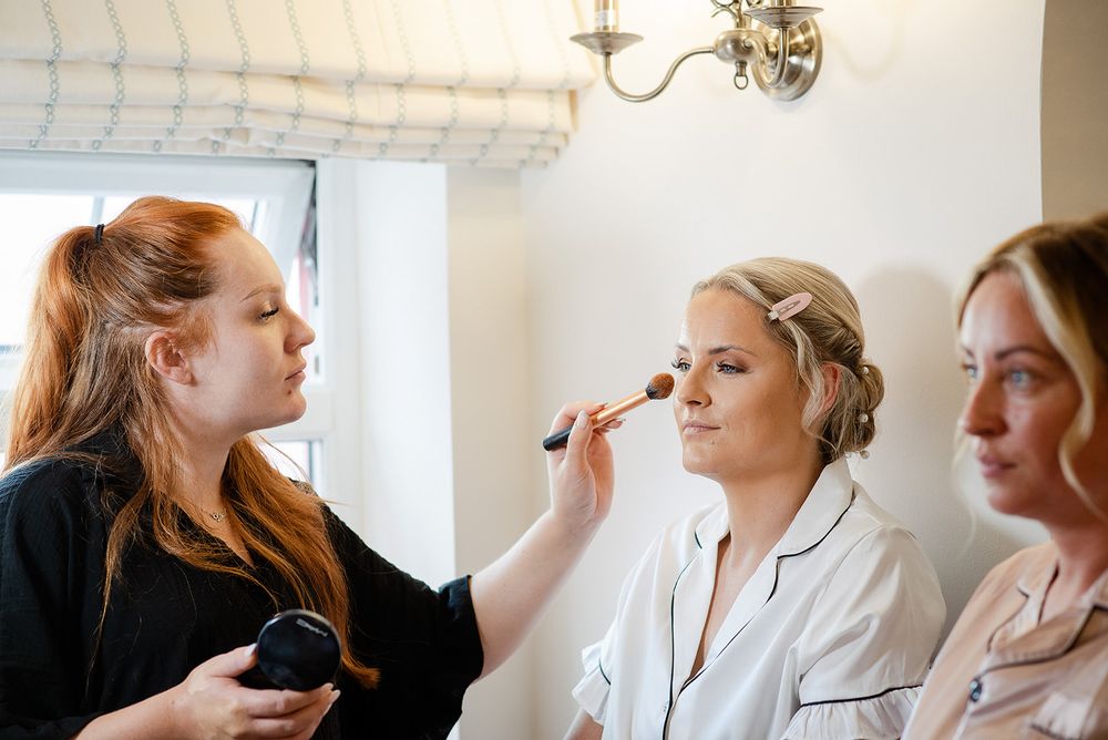 Makeup artist applies cosmetics to bride during wedding day preparations.