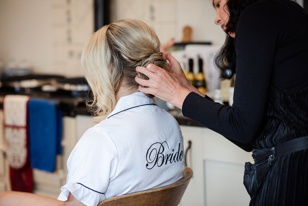Hairstylist styling bride's hair while wearing customized robe.