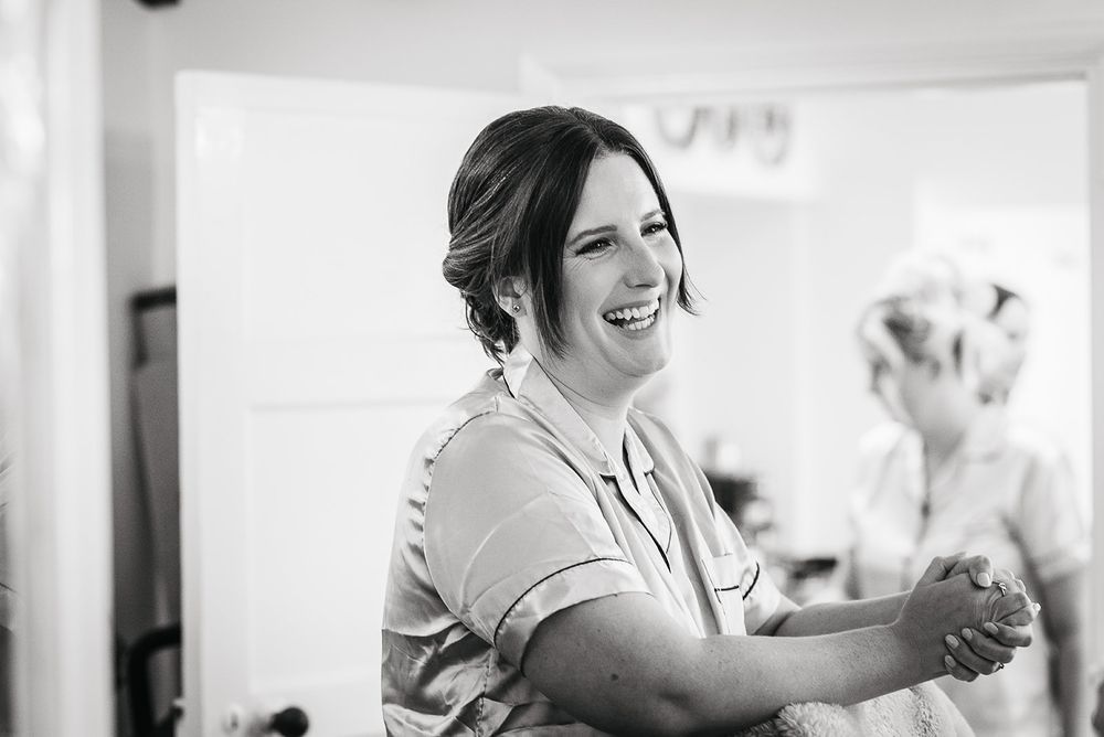Black and white candid photo captures joyful laughter during wedding preparations.