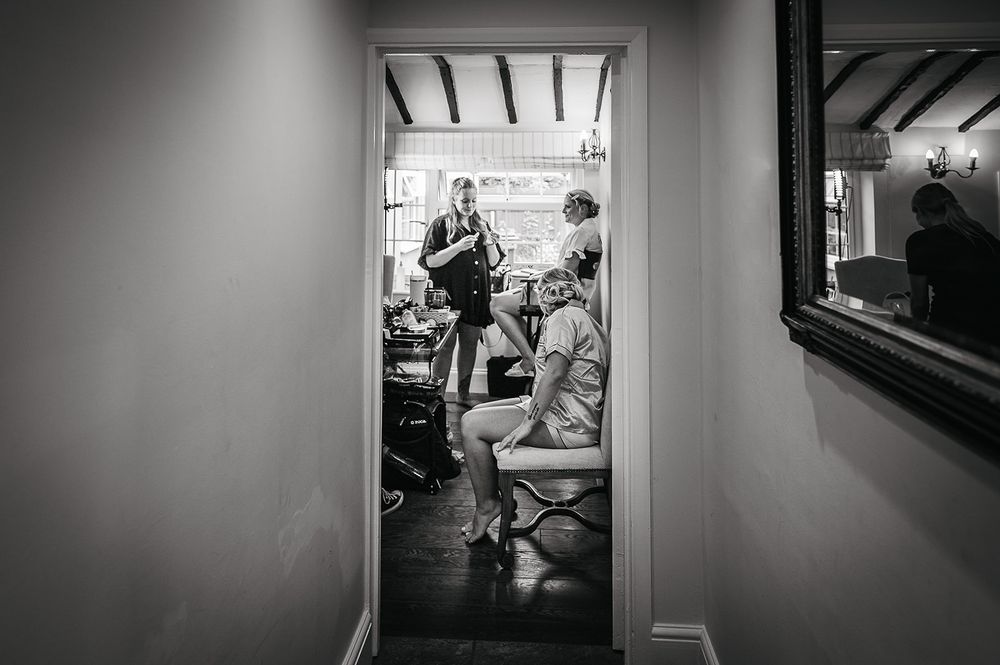 Black and white photo showing wedding preparations through doorway and mirror reflection.