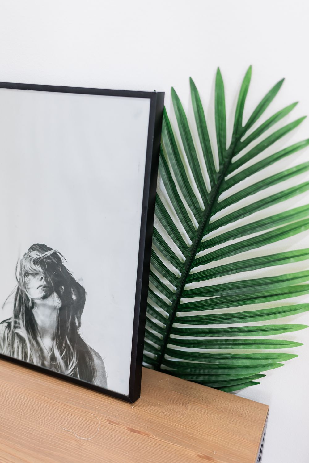 Black and white portrait displayed next to vibrant green palm frond on wooden surface.