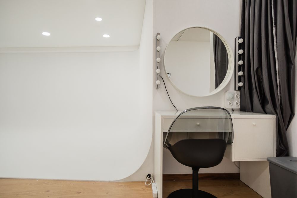Modern dressing room setup with round vanity mirror and black chair against white walls.