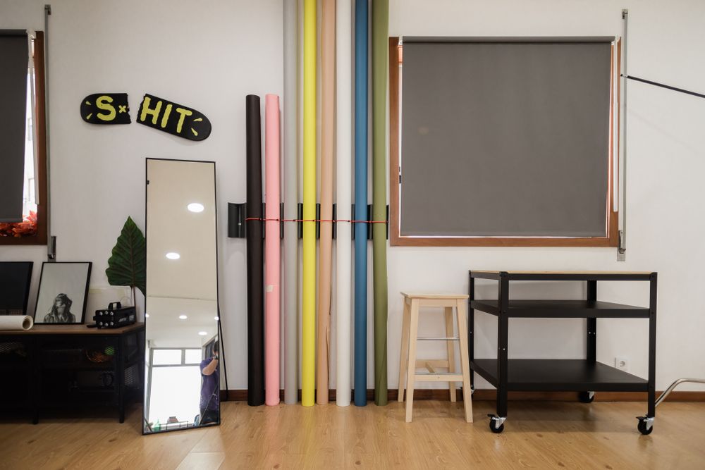 Studio space with colorful vertical poles, mirror, and black furniture against a white wall.