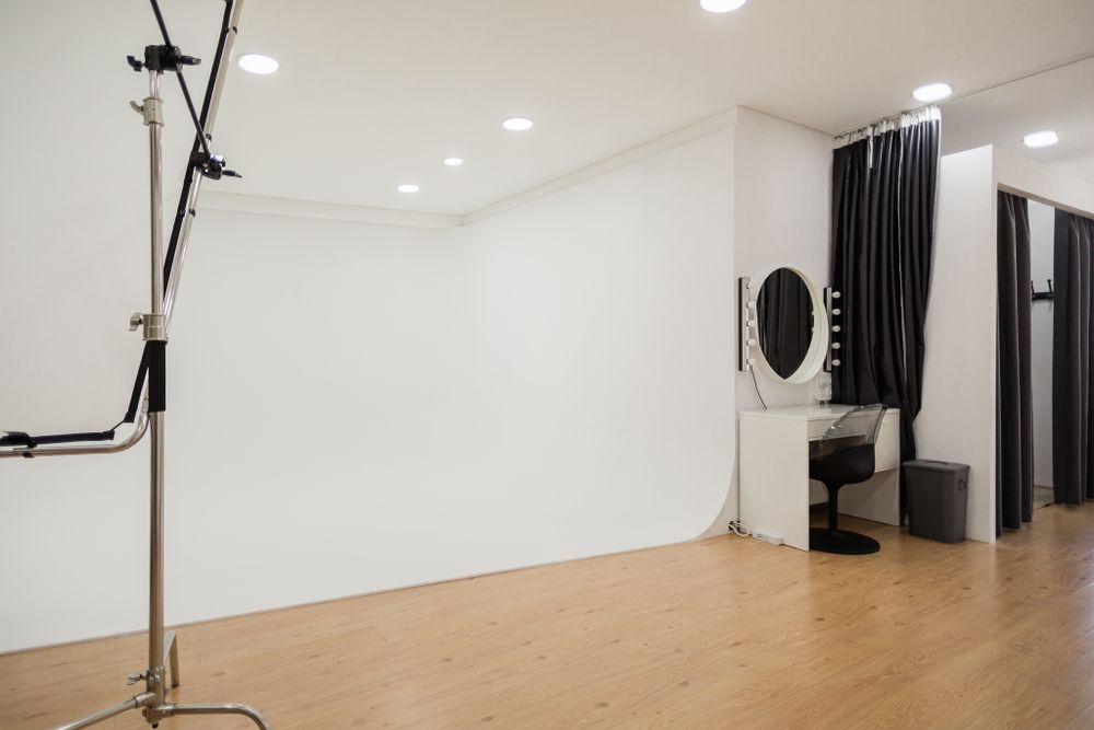 Professional photo studio with white walls, dark curtains and wooden flooring with studio lighting equipment.