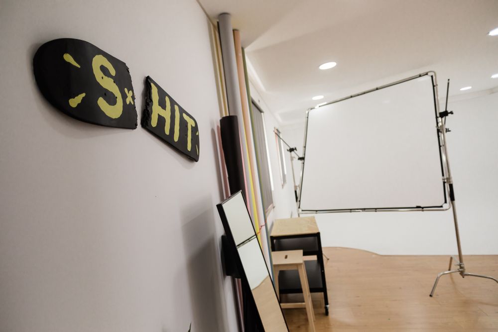 Photography studio interior with white backdrop stand and 'S Hit' sign on the wall.