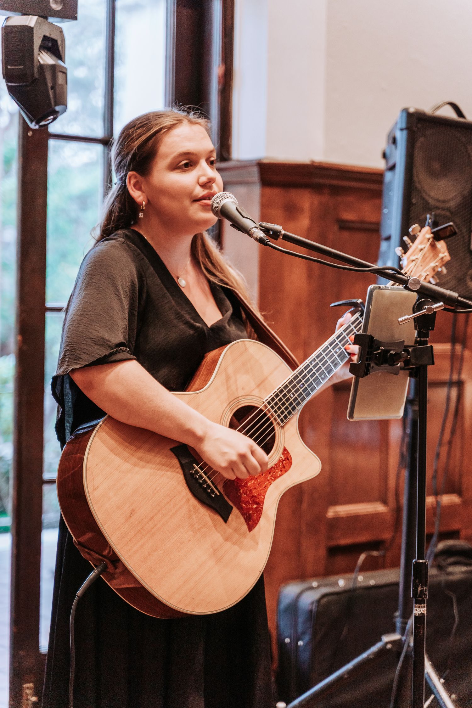 Musician performs with acoustic guitar in front of microphone setup during event.